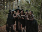 Group of women dressed as witch coven reading spell book in forest