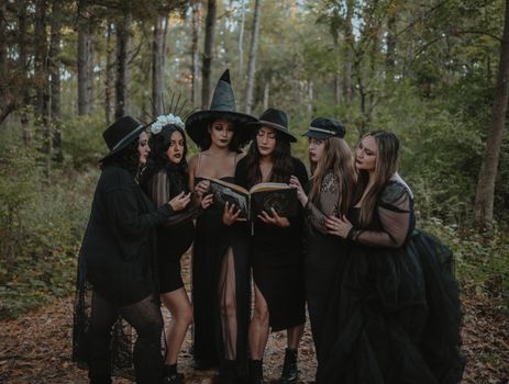 Group of women dressed as witch coven reading spell book in forest