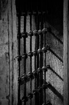 Black and white photo of an old barred window with dramatic shadows.