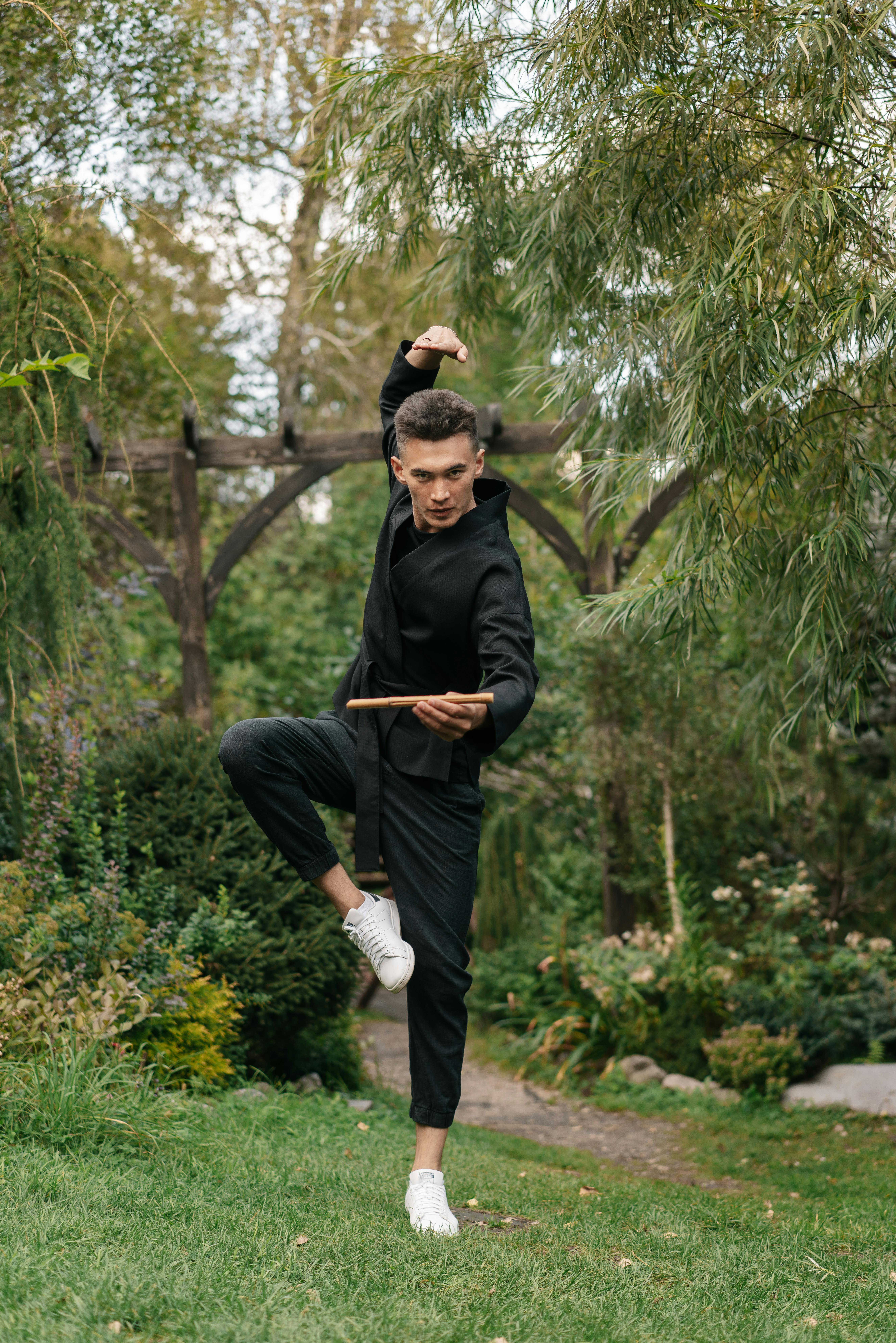 Martial artist performing a pose with a stick in a vibrant garden, showcasing strength and balance.