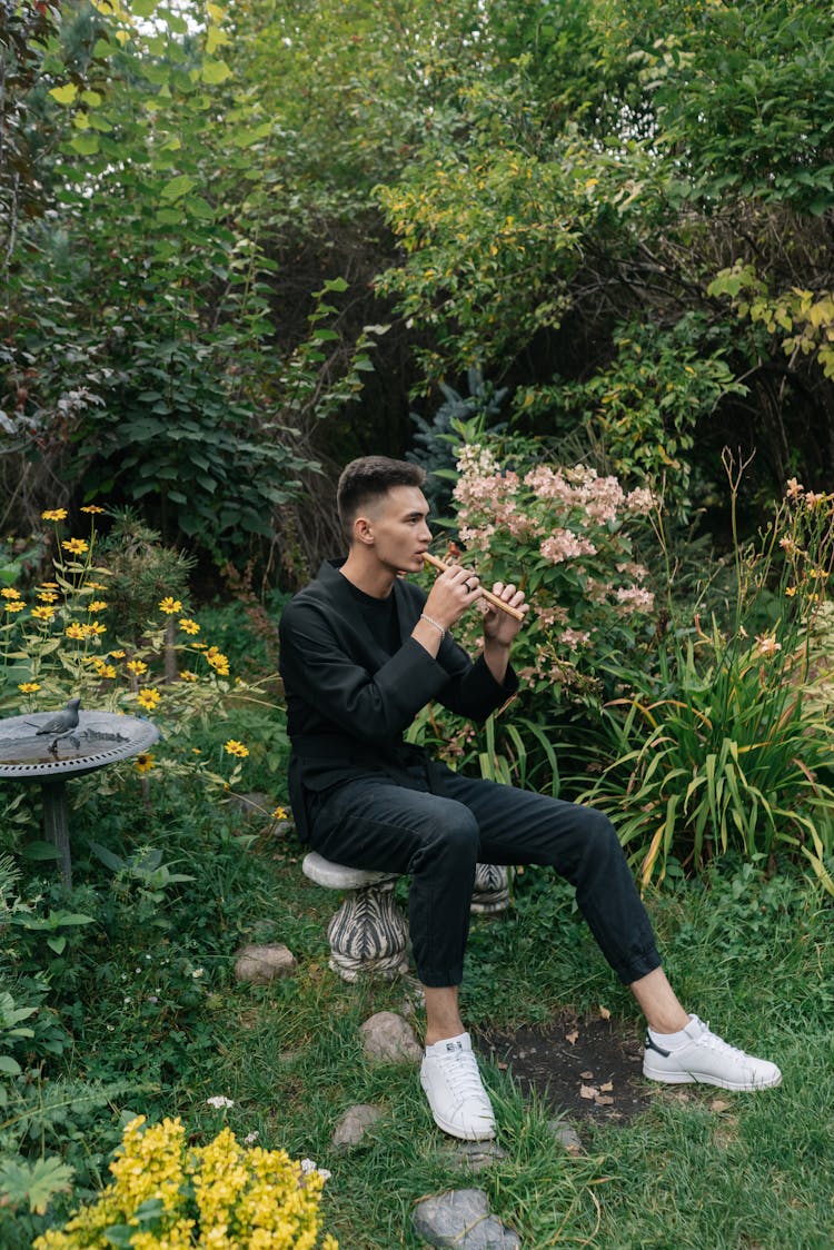 A Man Sitting In A Garden While Playing The Flute