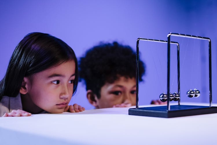 Boy And Girl Looking At Newton S Cradle And Hiding Behind The Table