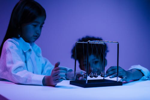 Free Boy and girl playing with newton s cradle in a blue light Stock Photo