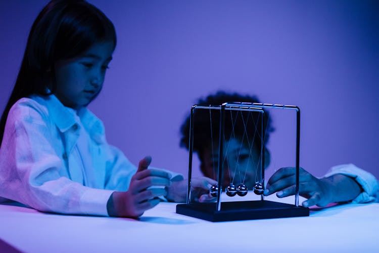 Boy And Girl Playing With Newton S Cradle In A Blue Light