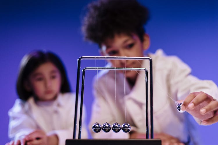 Boy And Girl Making Move A Ball Of Newton S Cradle
