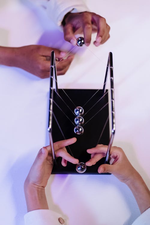 Unrecognizable hands of two young people playing metal balls of Newtons cradle