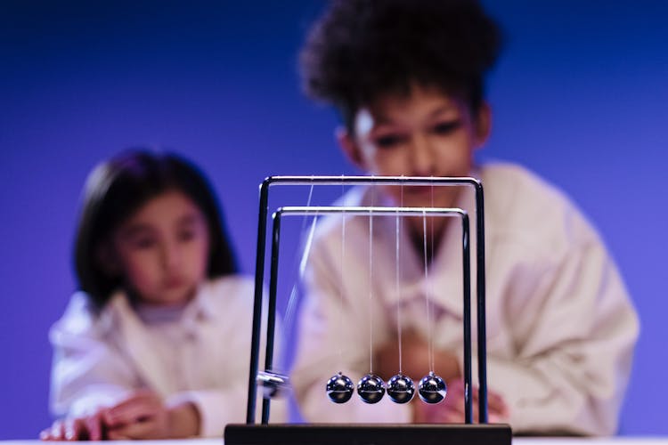 Boy And Girl Observing Balls Of Newton S Cradle Moving