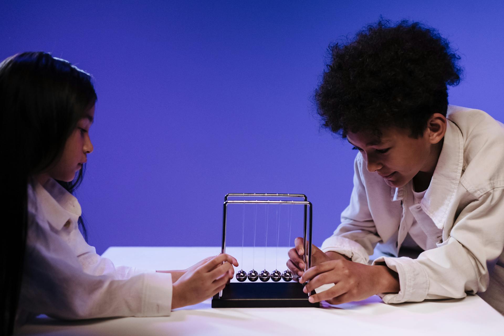 Two kids explore Newton's cradle, learning science in a studio setting.