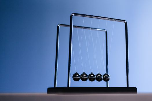 Silhouette of Newton's cradle with metallic balls against a blue background, showcasing physics in action.