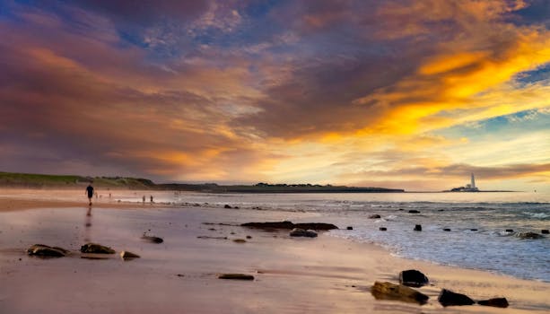 A breathtaking sunset over a tranquil beach with a dramatic sky and distant lighthouse.