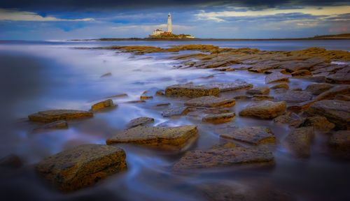 Free Captivating view of St. Mary's Lighthouse at dawn with rocky shoreline and serene sea. Stock Photo
