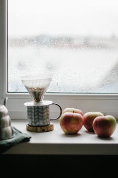 Warm and inviting scene of drip coffee and fresh apples on a rainy windowsill.