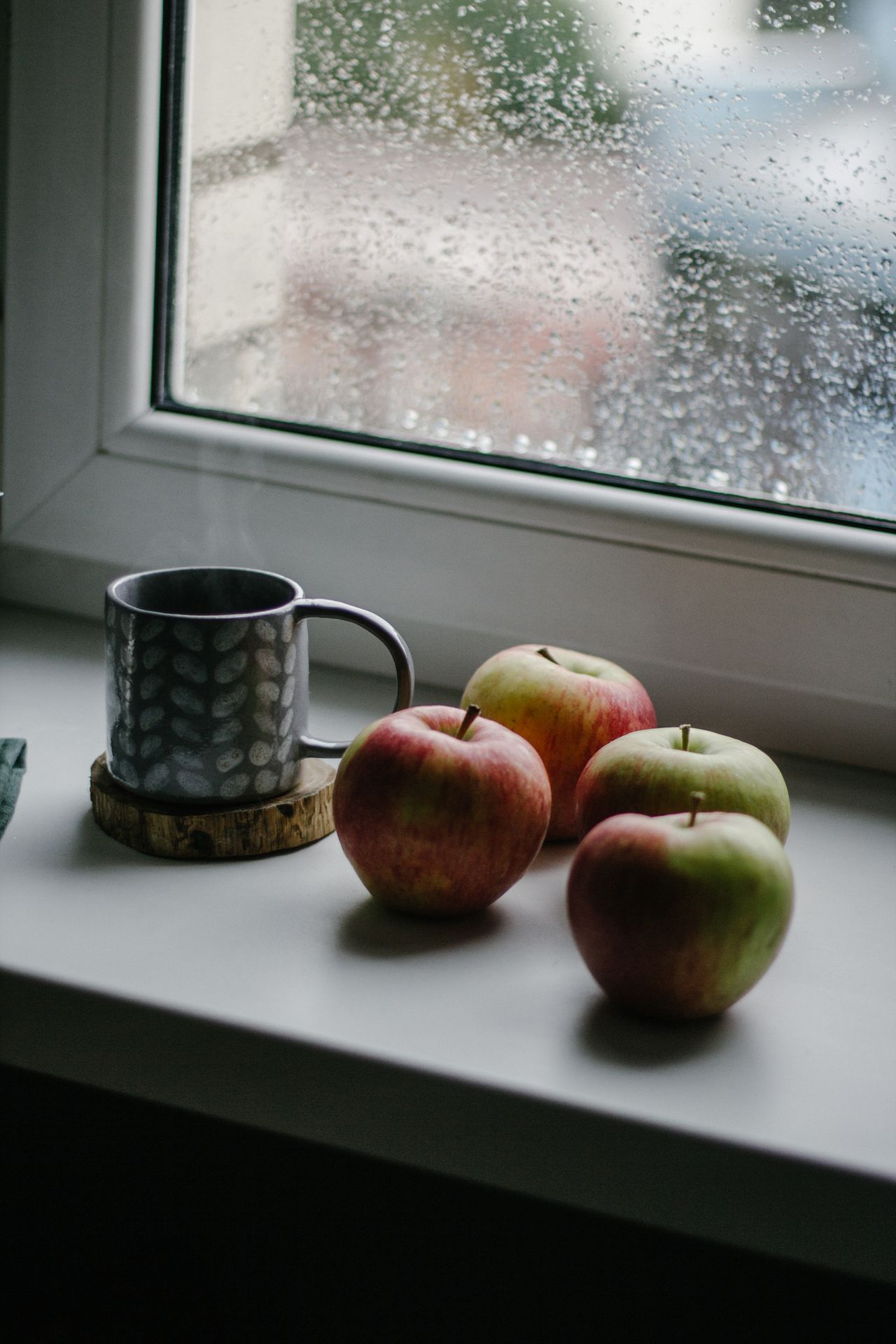 Steaming mug with fresh apples on a rainy windowsill