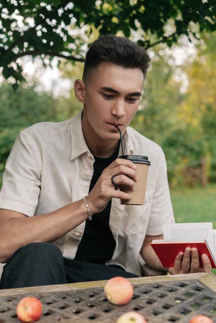 Man Sitting By The Metal Garden Table Drinking On Take Out Coffee Cup