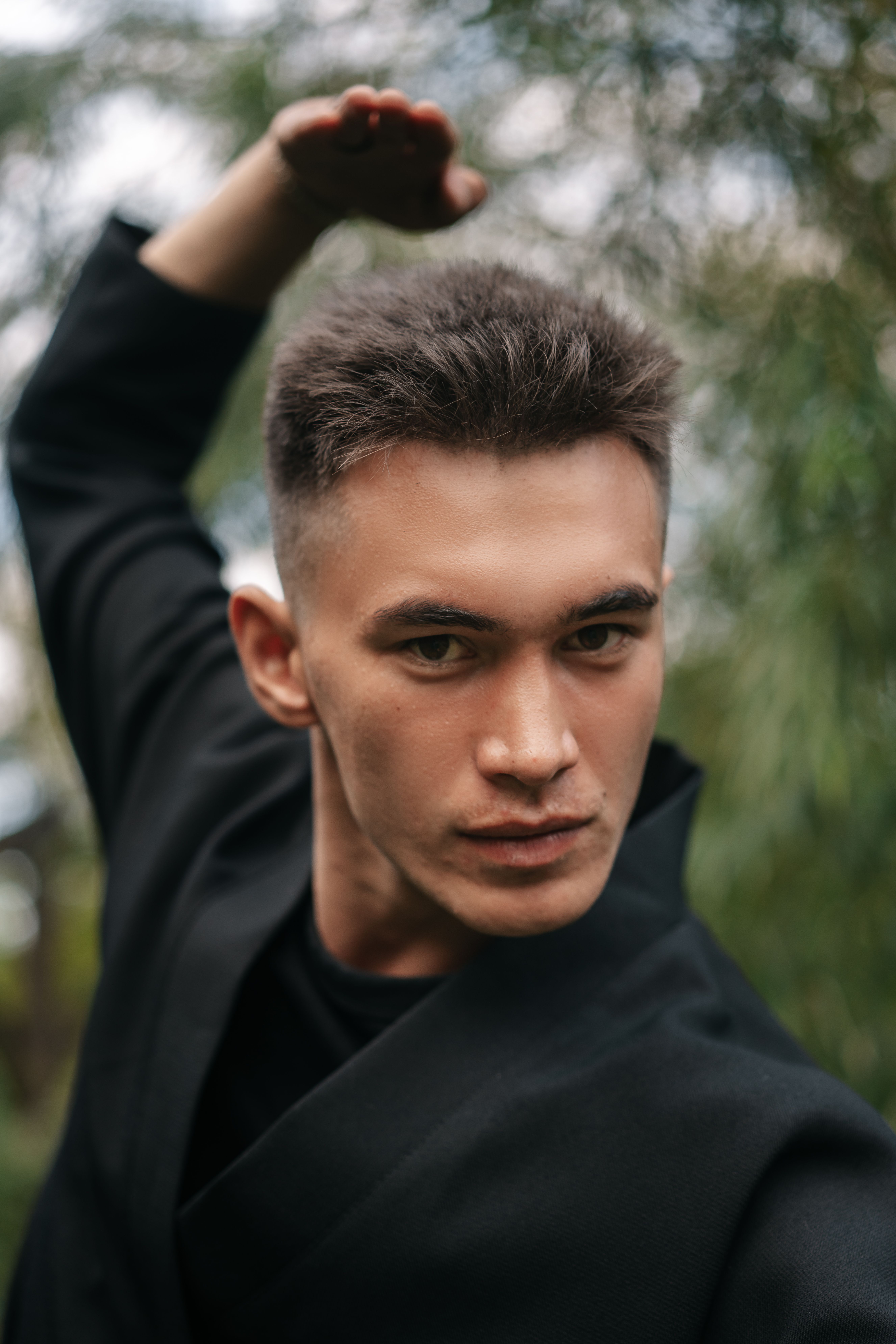 Young man posing in a black kimono outdoors, expressing martial arts confidence and style.