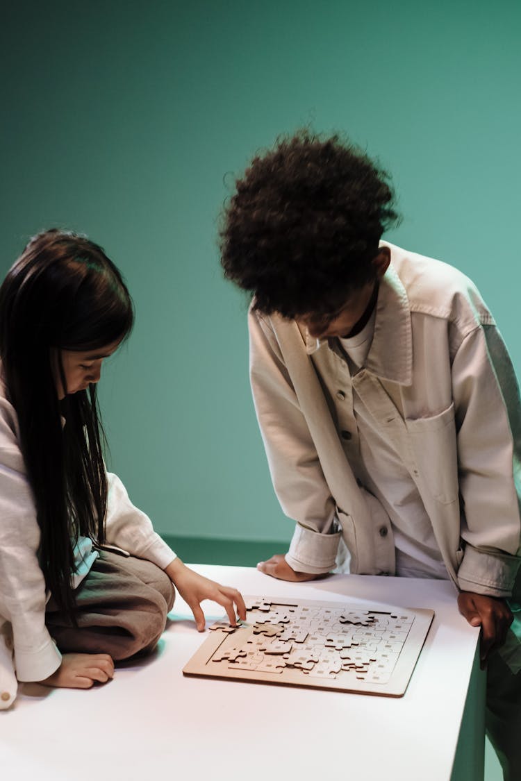 Two Kids Leaning Over Puzzle Laying On Table