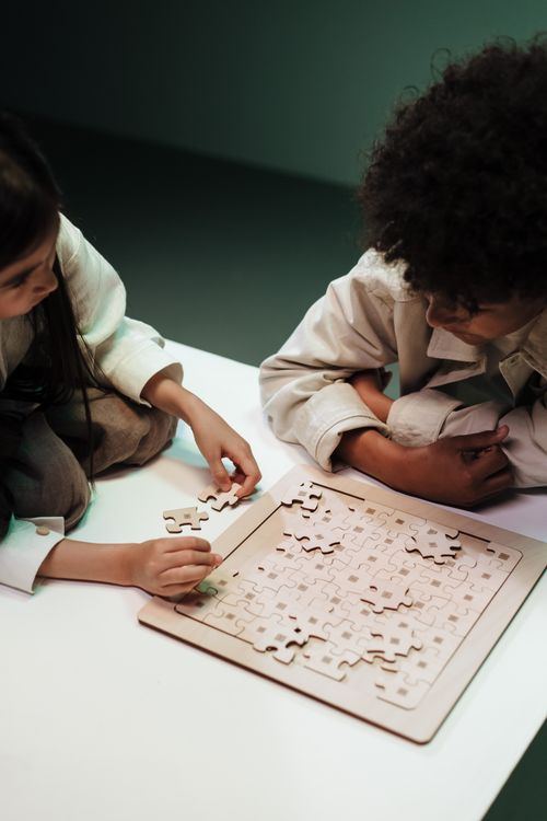 Free Two children solving a jigsaw puzzle together, focused on teamwork and intellectual development. Stock Photo