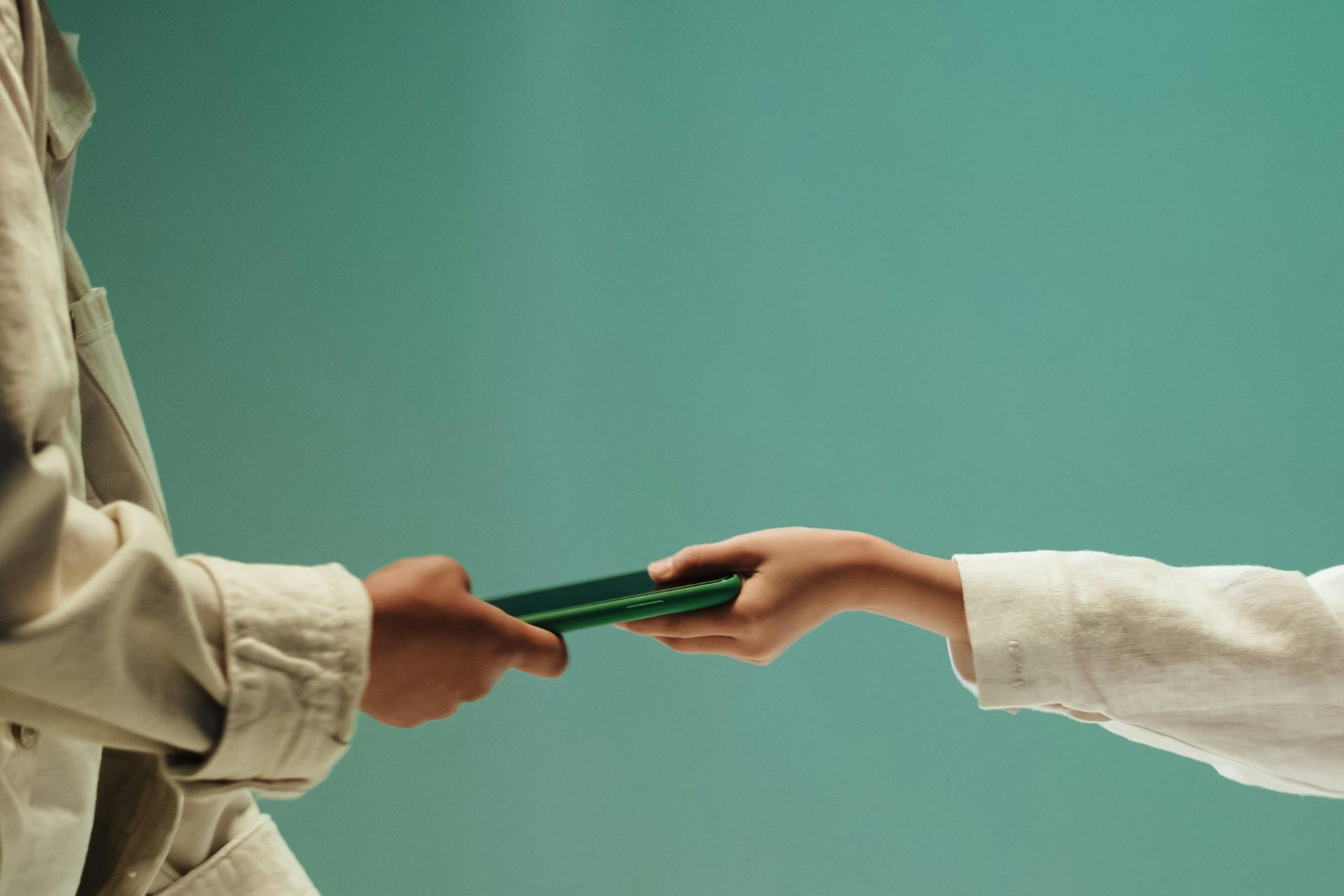 Unrecognizable hands of two teenagers holding green mobile phone