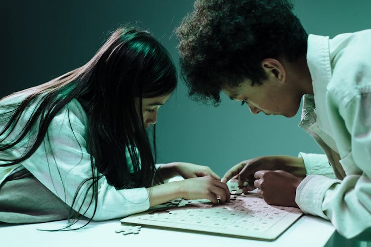 Teenage Girl And Boy Doing Jigsaw Puzzles Laying On Table