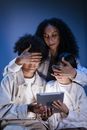 Mother covering eyes of her children with hands against internet content on digital pad