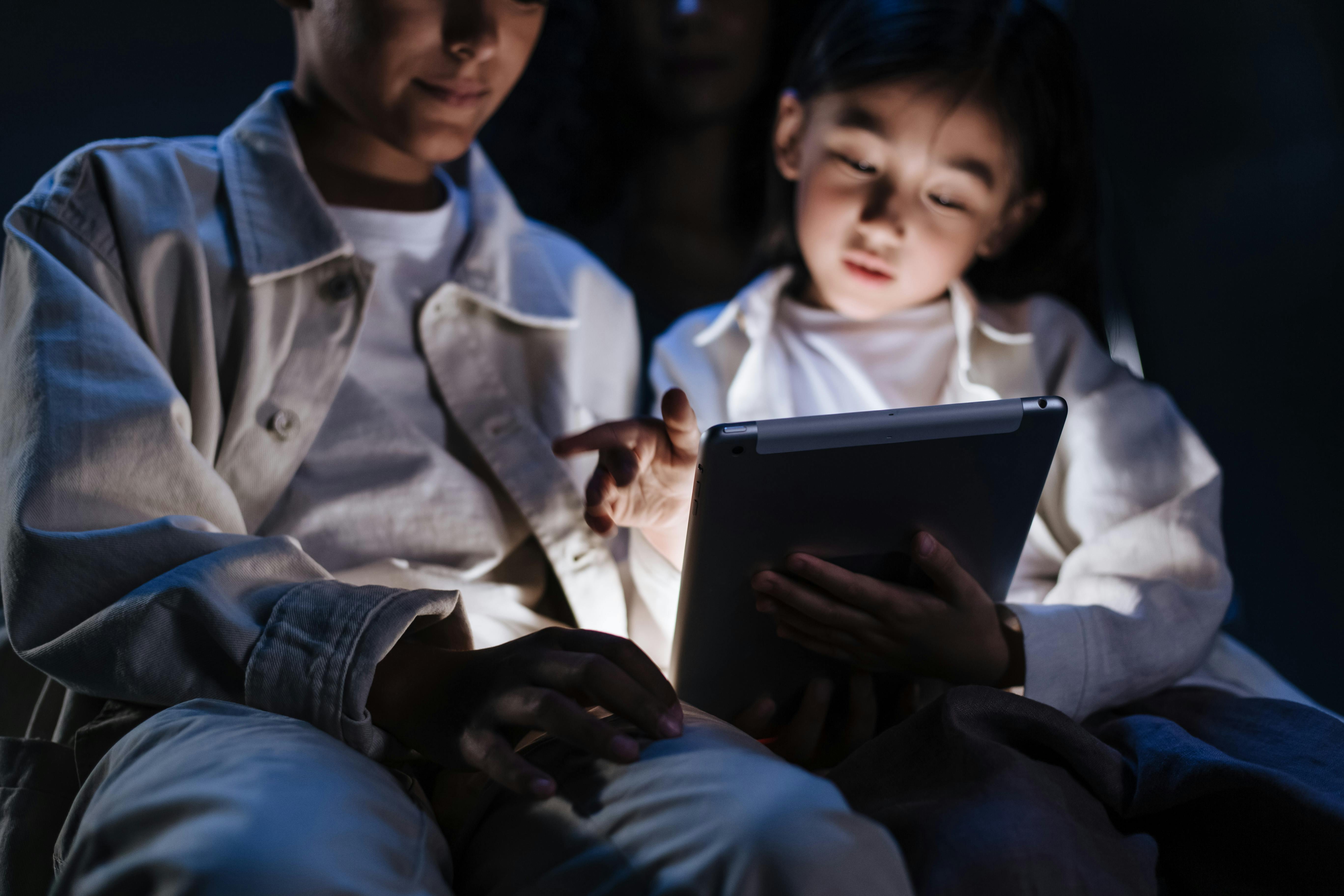 two kids sitting in dark room and looking to digital pad