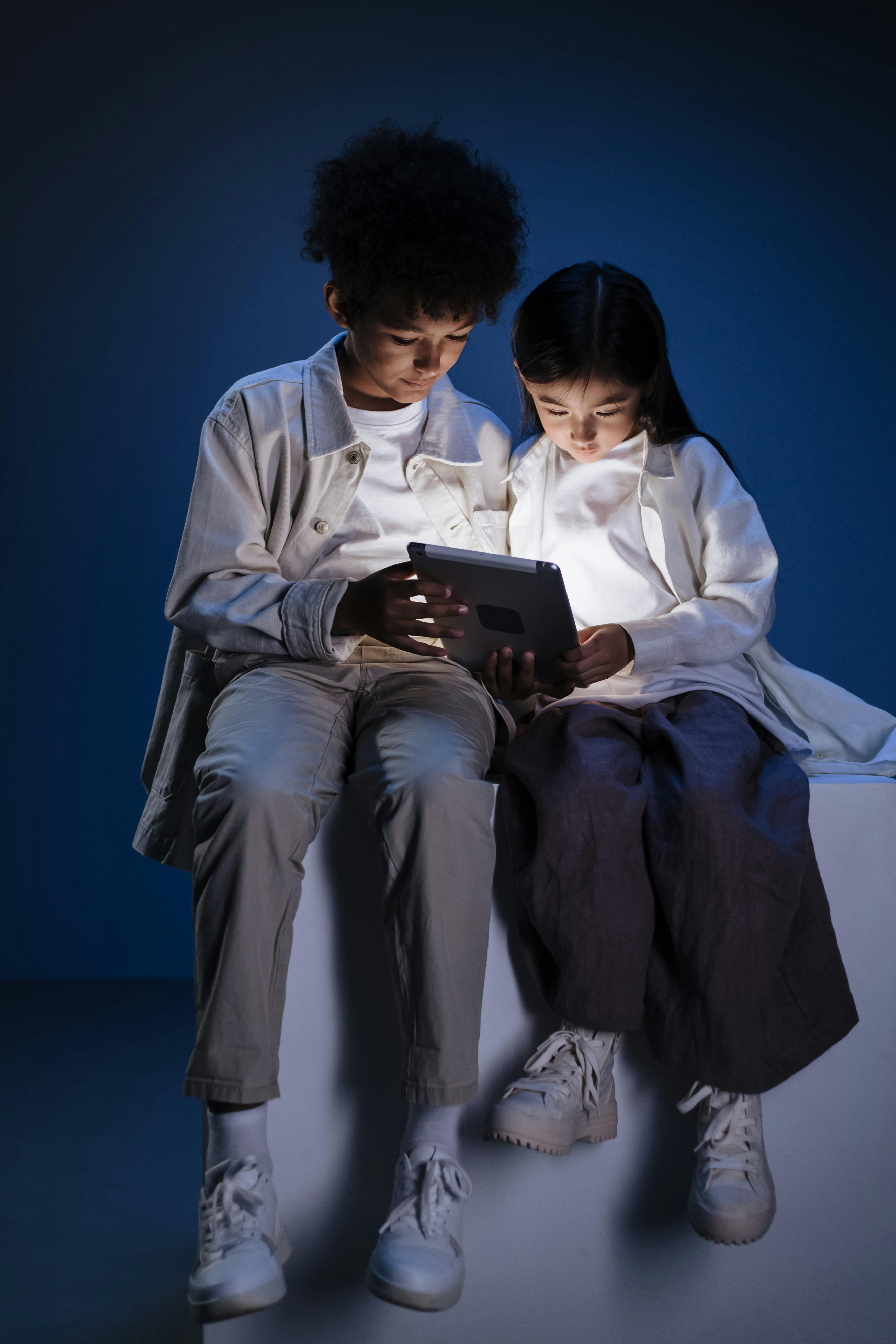 brother and sister sitting together on podium and reading from digital pad