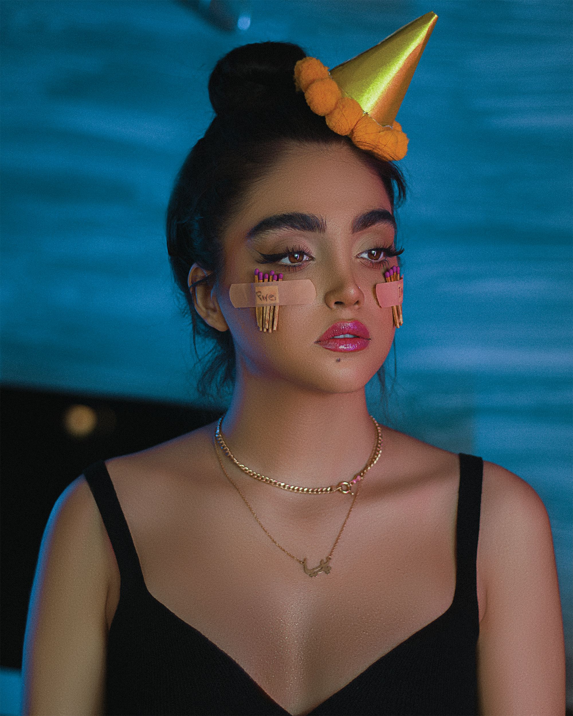 Portrait of a fashionable young woman with creative makeup and party hat indoors.