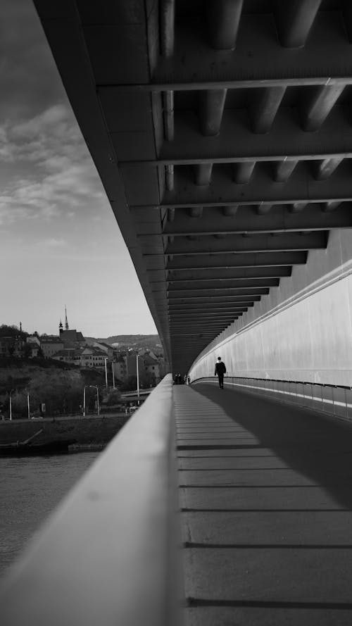 Black and White Photo of a Person Walking on the Bridge