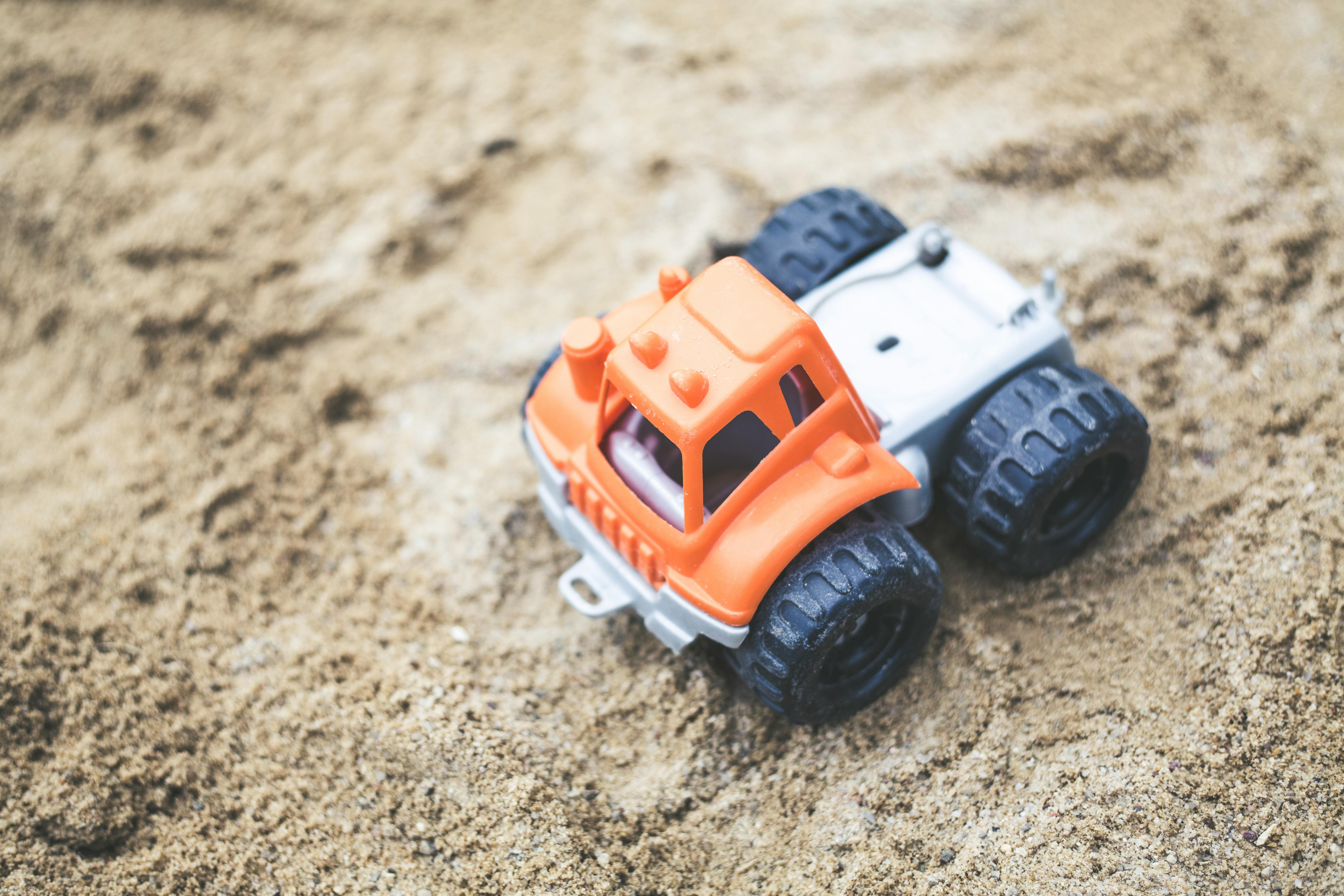 A vibrant orange toy truck sits on a sandy surface, showcasing playful outdoor fun.