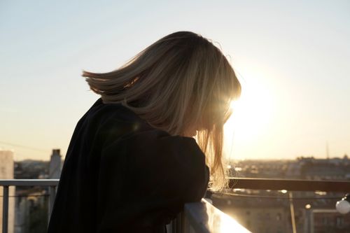 Free A woman with blonde hair gazes over a railing at sunset, creating a backlit silhouette. Stock Photo
