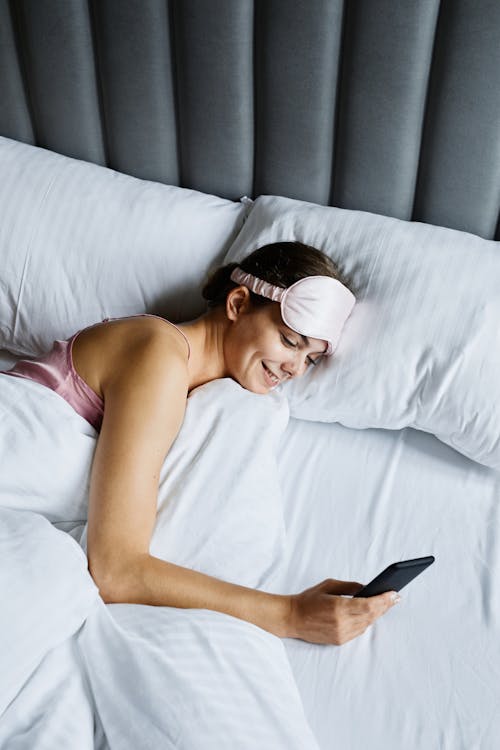 Free A Woman Using a Mobile Phone while Lying in the Bed Stock Photo