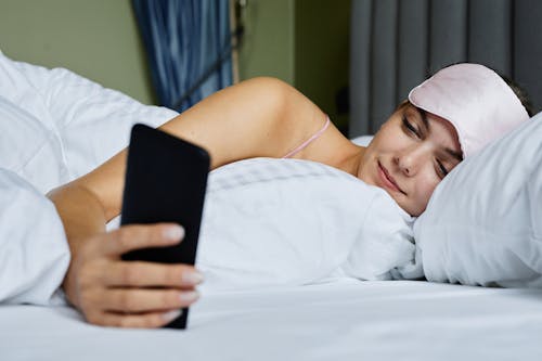 Free A Woman Using a Mobile Phone while Lying in the Bed Stock Photo