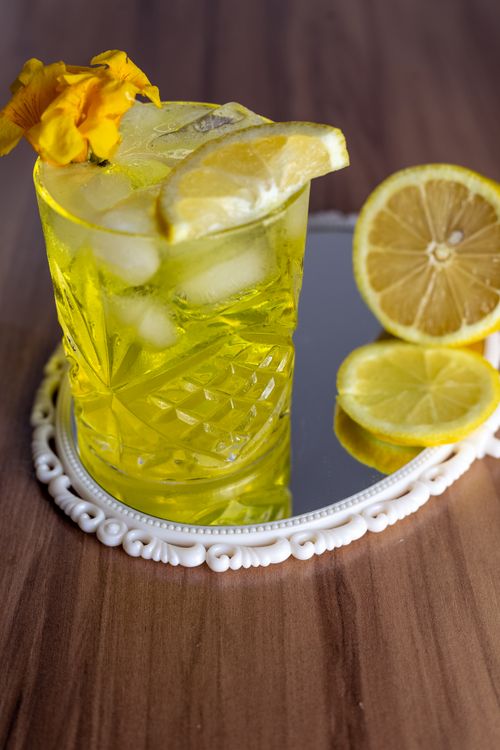 Free Vibrant yellow lemonade with ice cubes and lemon slices in a decorative glass on a wooden table. Stock Photo