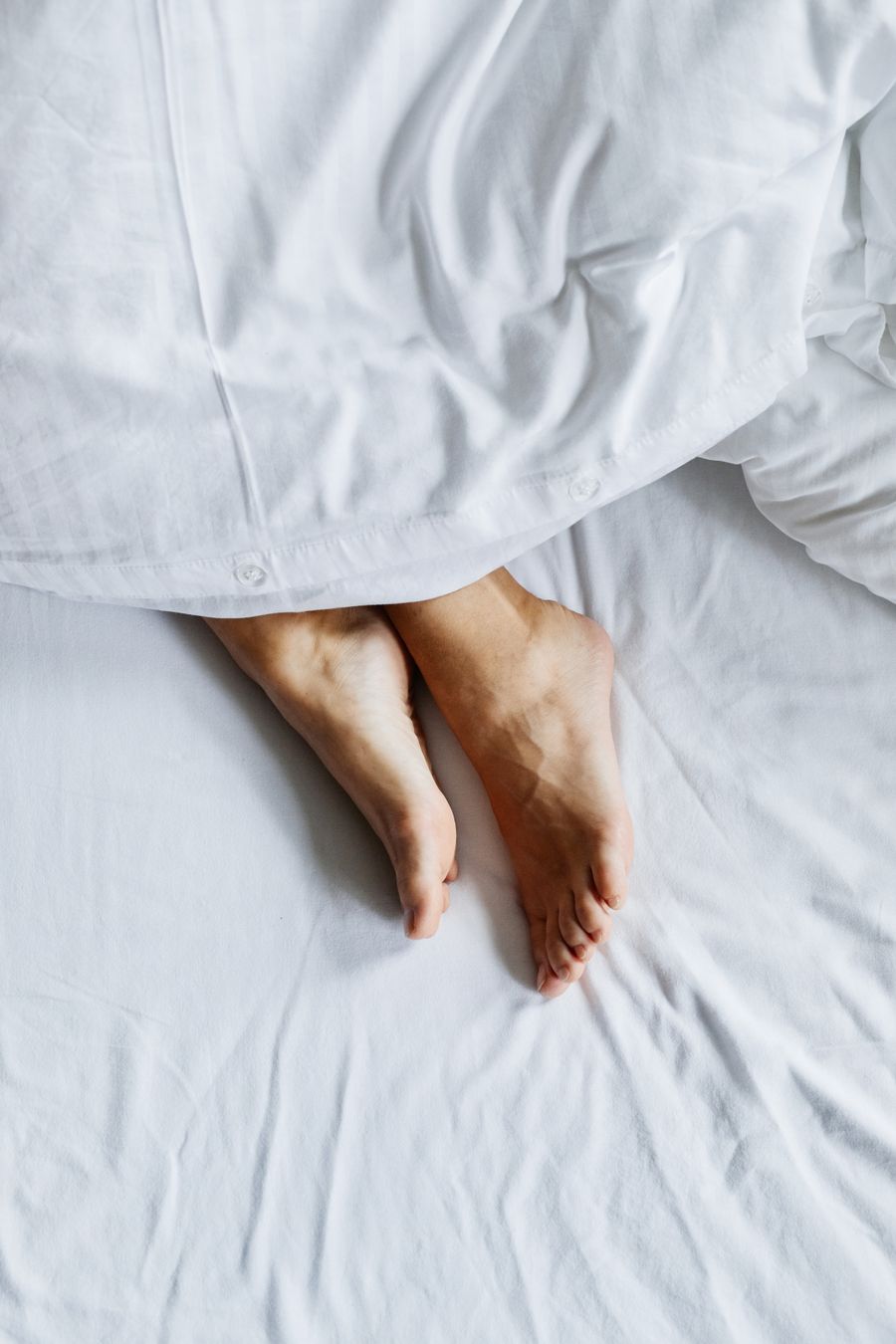 Bare feet resting on white bedsheets at night, illustrating the burning feet of peripheral neuropathy