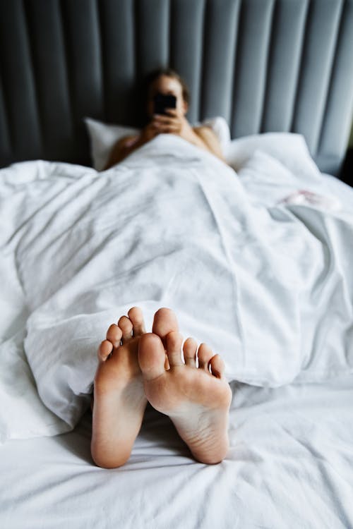 Free Person Using Her Smartphone While Lying on the Bed Stock Photo