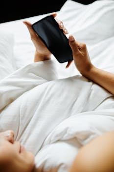 Close-up of a person using a smartphone while relaxing in bed, providing a cozy and modern lifestyle vibe.