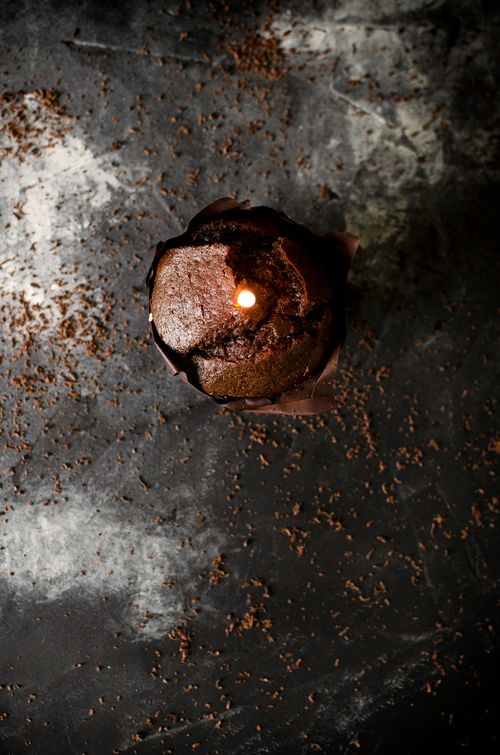 Free An artistic overhead shot of a chocolate muffin with a lit candle on a dark textured surface. Stock Photo
