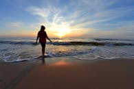 日落时分，一位女子沿着海滩散步，营造出宁静的氛围