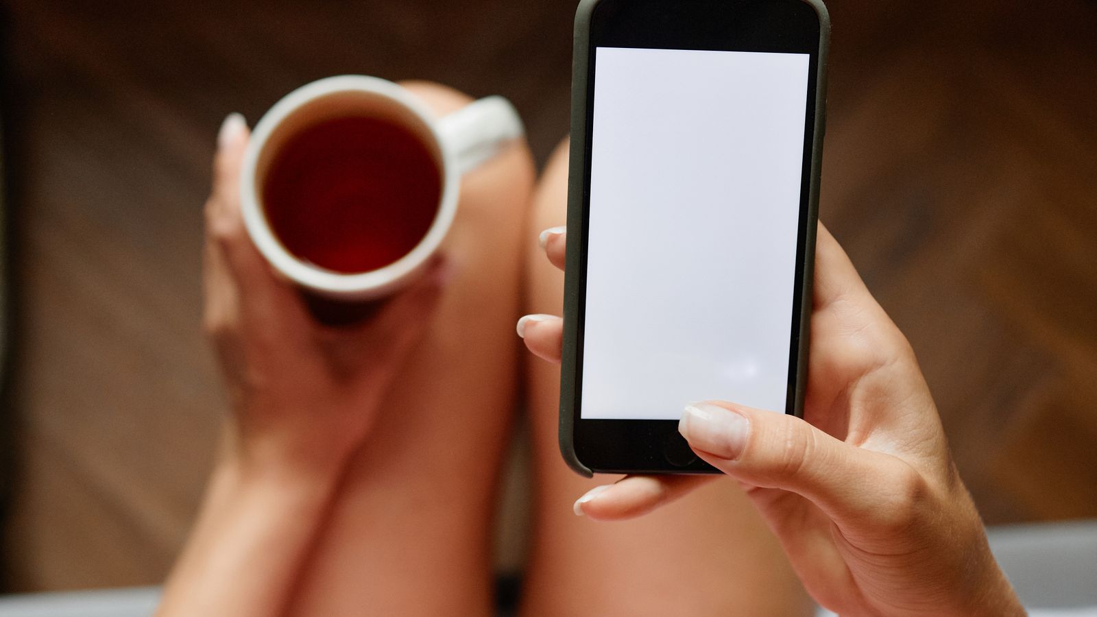 Hands holding a cup of tea and a smartphone with a blank screen