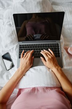 Overhead shot of a woman using a laptop on a bed, showing relaxed lifestyle.