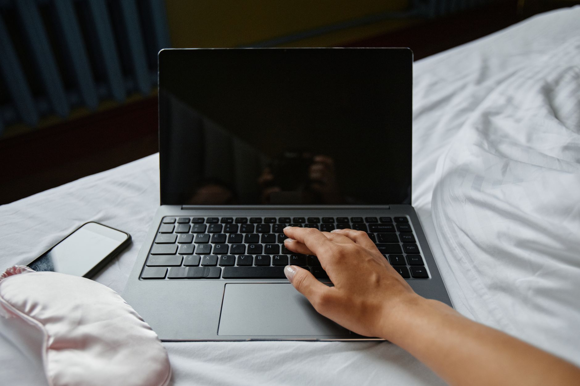 手機海外寄明信片地址管理:多語輸入技巧全攻略 A hand resting on a laptop keyboard beside a phone and eye mask on a bed.