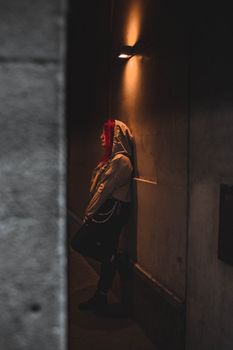 Moody portrait of a person with red hair leaning on a wall in a dark urban setting.