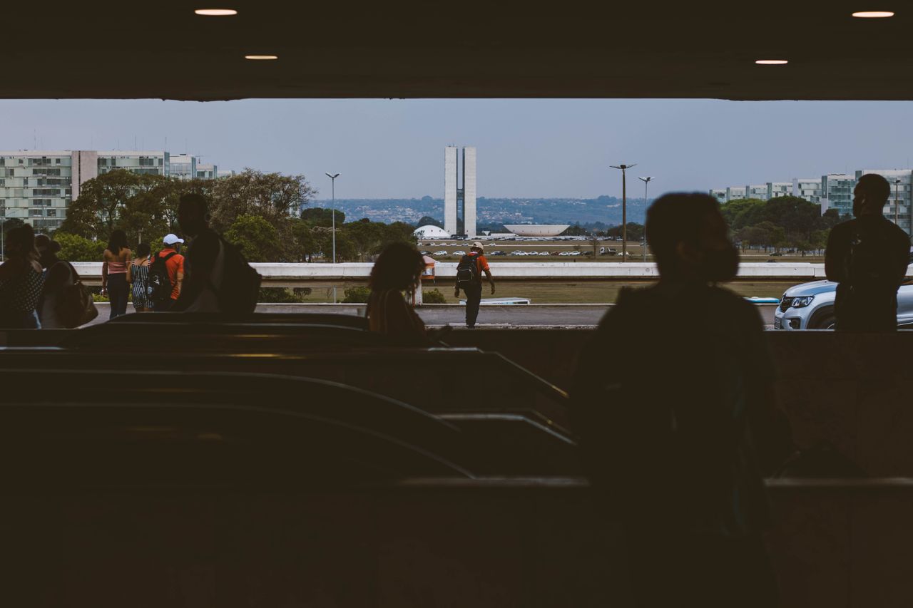 Silhouettes of people in an underpass with Brasília's National Congress in the background.
