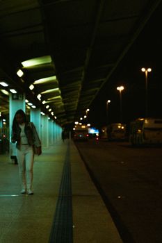 A woman standing at a Brasília bus station at night, under glowing lights.