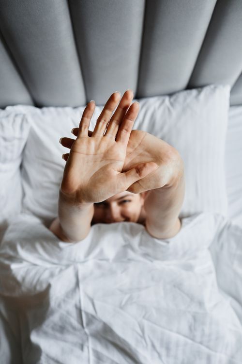 Free A woman stretches her arms while lying in bed, surrounded by soft pillows and a cozy atmosphere. Stock Photo