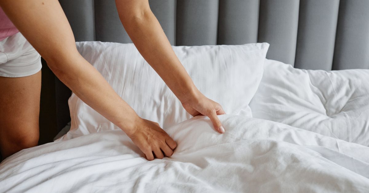 Troca da roupa de cama Mãos de mulher arrumando a cama com lençóis e travesseiros brancos