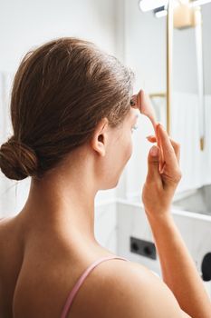 Woman using a facial roller for skincare in a modern bathroom setting.