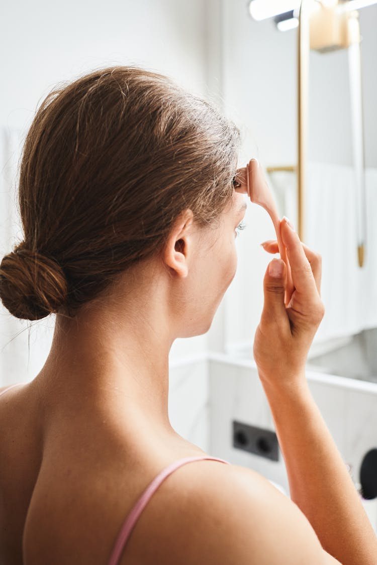 Back View Of Woman Using A Facial Massager 