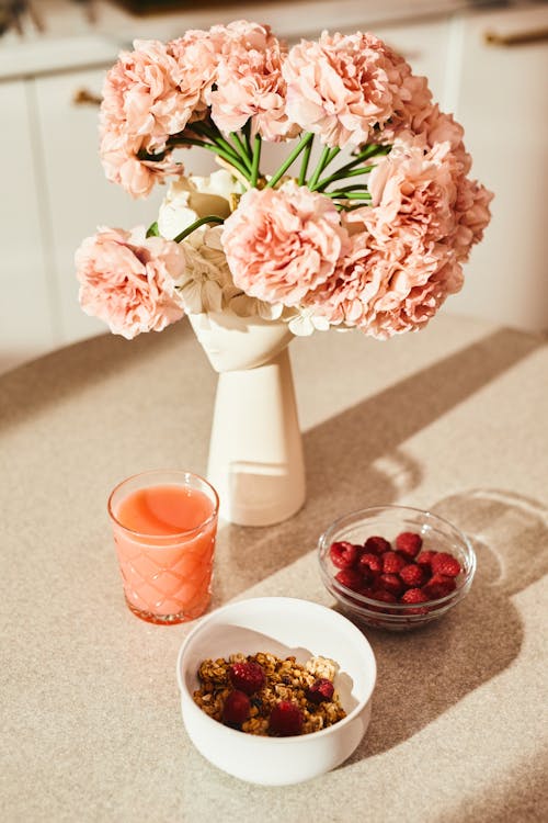Photo of a Vase with Flowers Near a Bowl with Raspberries
