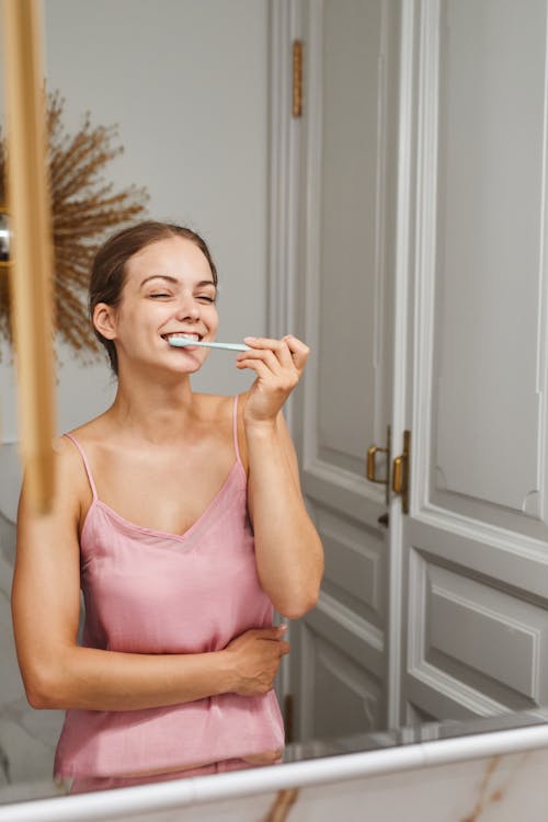 Free Woman in Pink Spaghetti Strap Brushing Her Teeth Stock Photo
